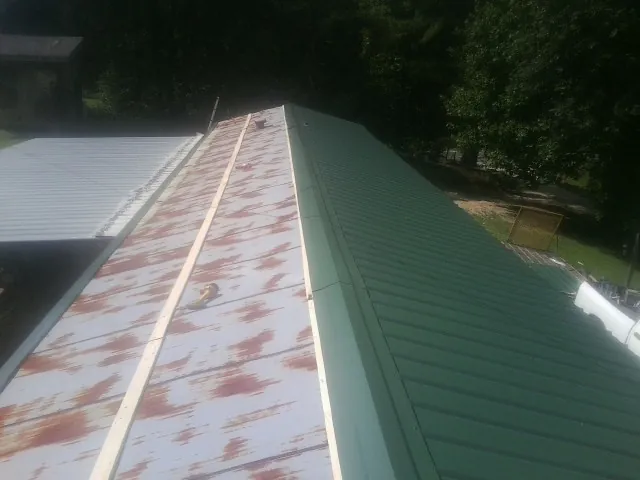 Old rusted panels beside newly installed green metal roofing — Wind Damage Roof Repair by Roofing Brothers in Eubank