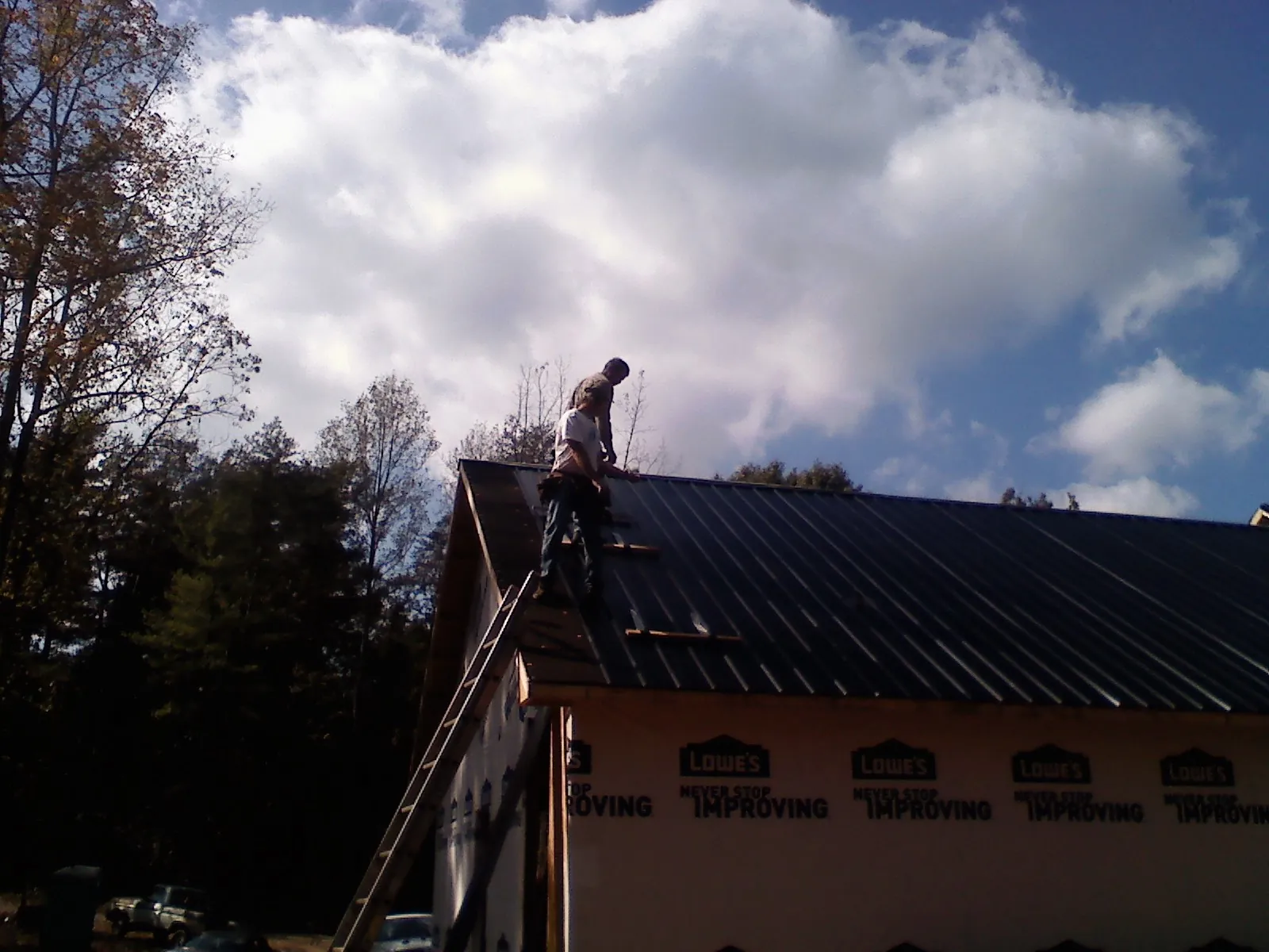 Roofer fastening dark metal panels high against a cloudy sky, from a Roof Inspection job in Eubank